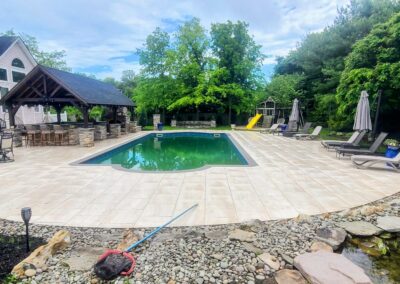 porcelain paver patio around the pool with outdoor kitchen fireplace and firepit