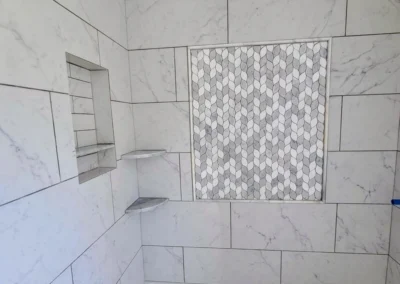 bathroom walls installed in 24X12 white tile with a shampoo box insert and corner shelf and a decoration in front wall